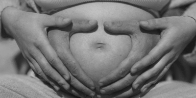 Raguénès Youna Femme enceinte assise en tailleur avec son partenaire, mains en cœur sur le ventre